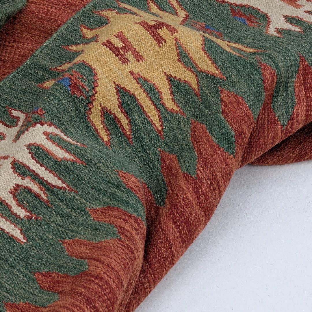 Handwoven kilim rug with geometric pattern in green, red, and yellow on white background