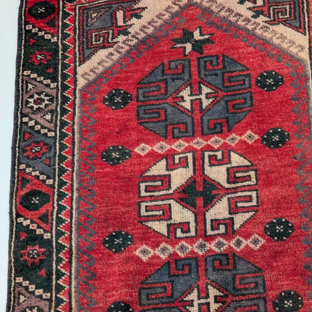 Red vintage Persian rug with geometric black and cream tribal patterns and border accents