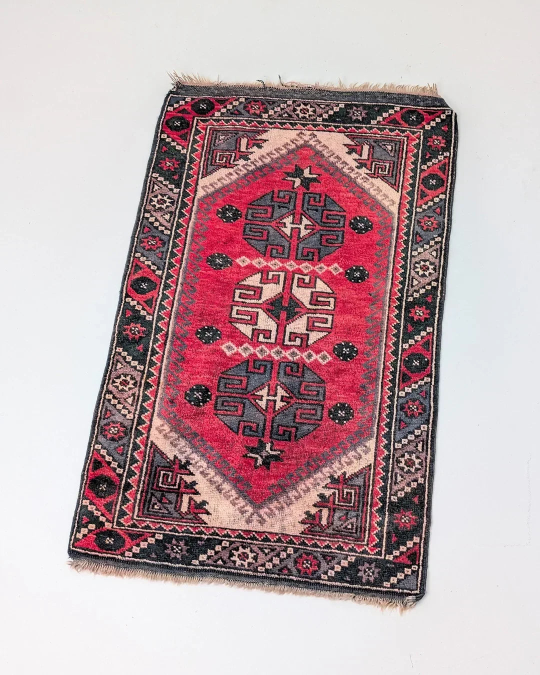 Red vintage Turkish rug with geometric patterns and decorative border on light background