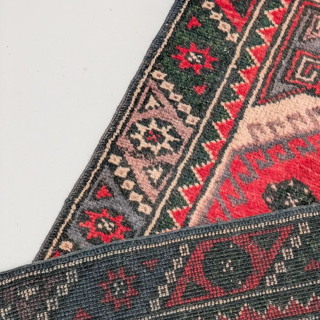 Colorful geometric patterned rug corner with red, green, and beige designs on a white background.