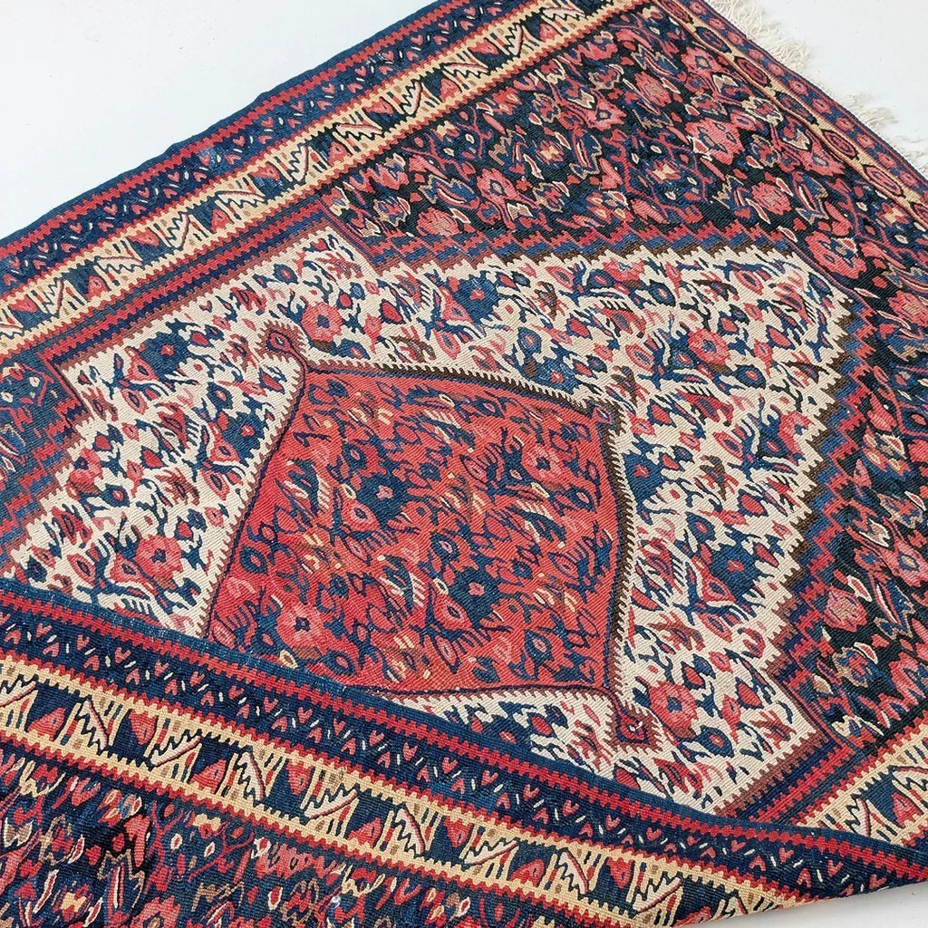 Vintage Persian rug with red, blue, and cream floral geometric pattern on white background