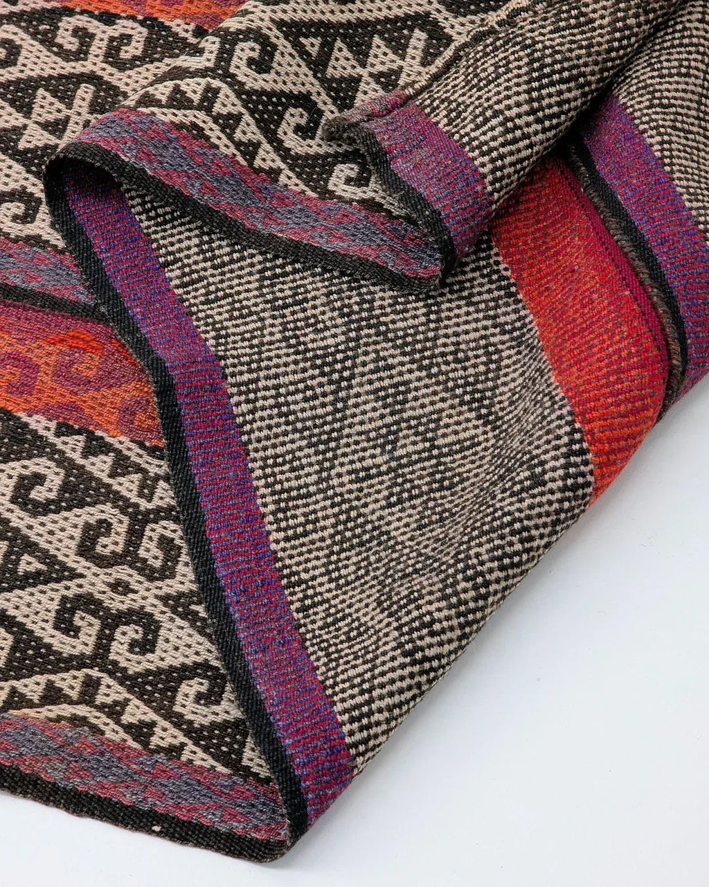 Handwoven textile with geometric black patterns and multicolor stripes on a white background