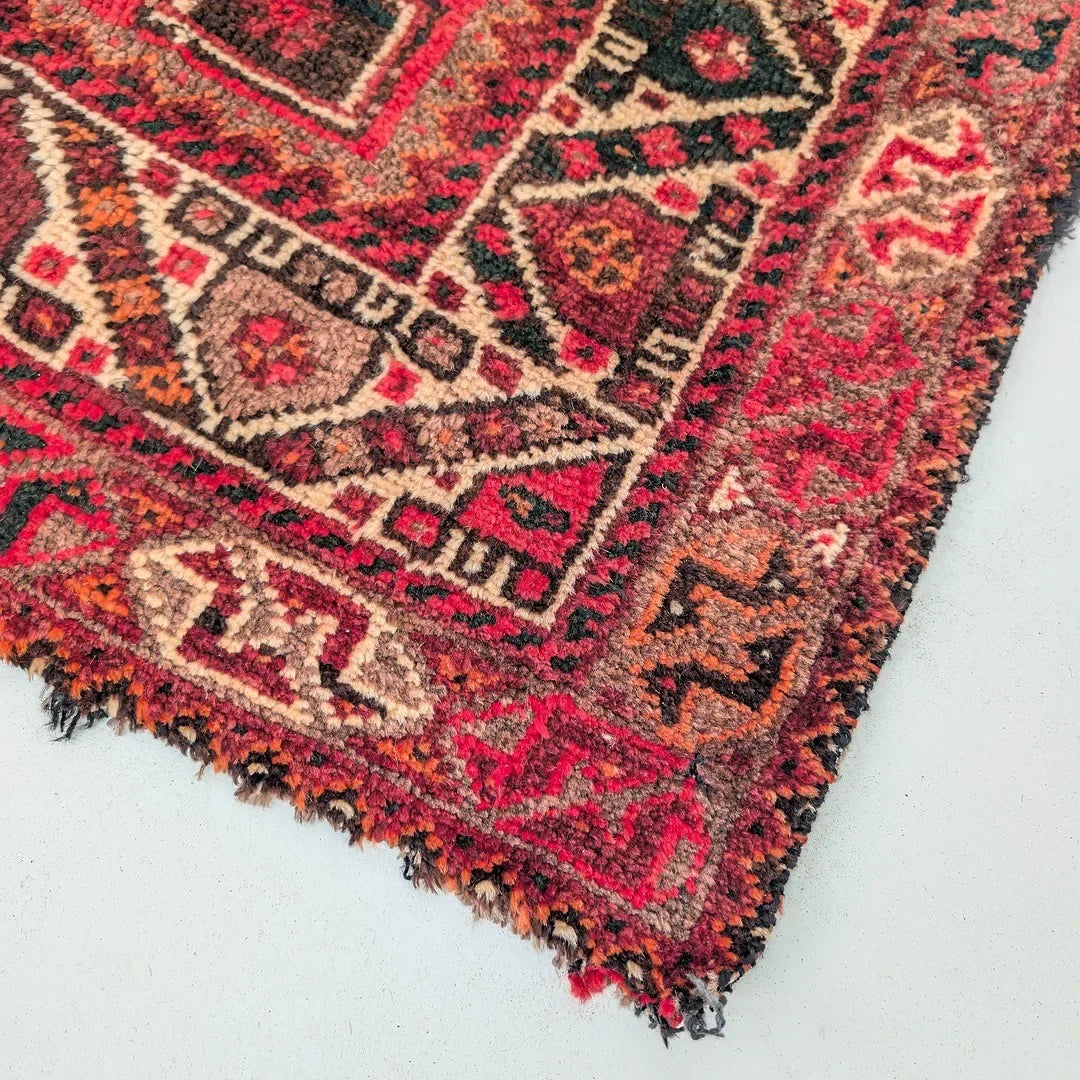Corner of a red vintage Persian rug with intricate geometric patterns on a light floor