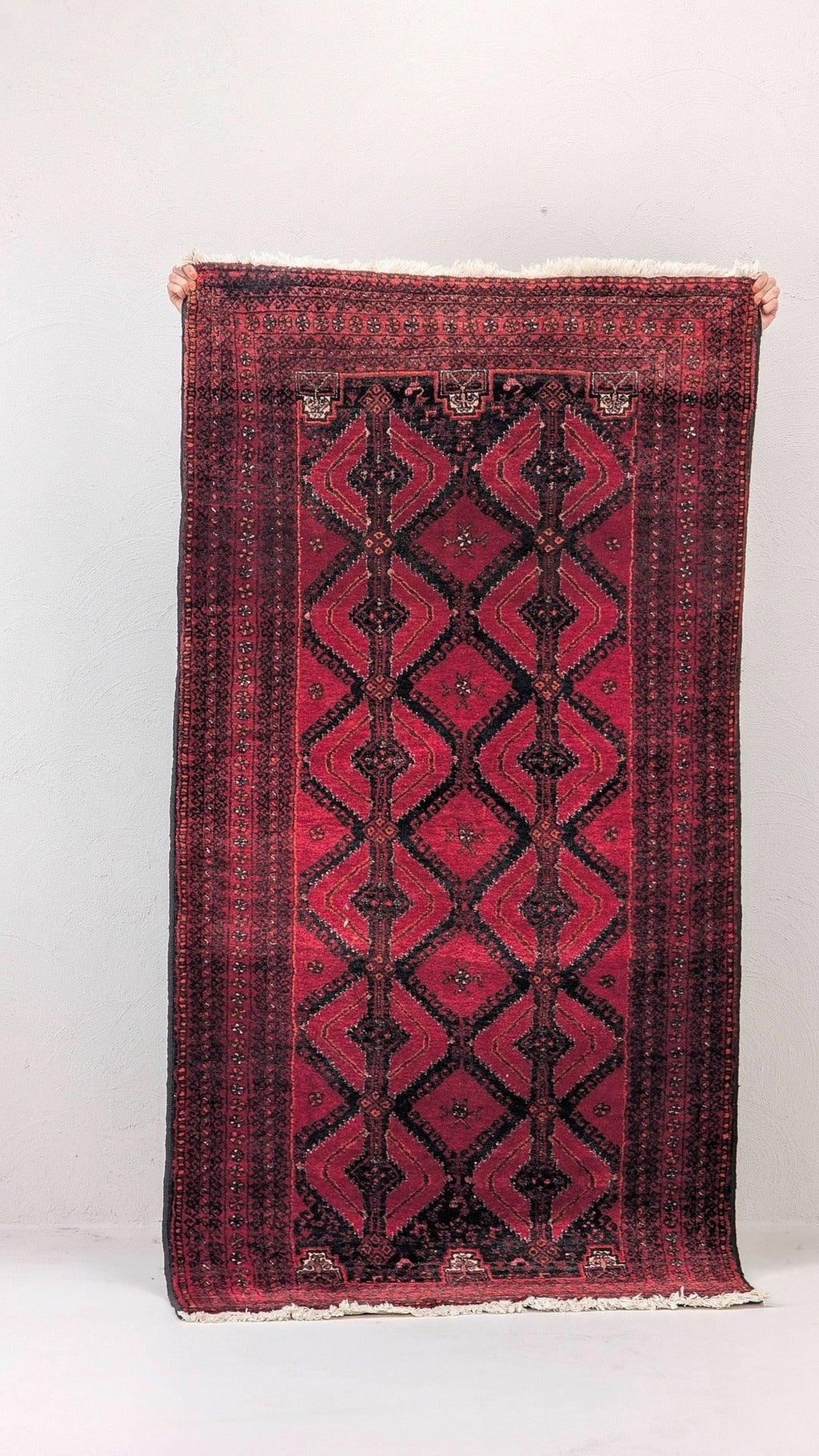 Hand holding vintage red Persian rug with geometric patterns against white wall