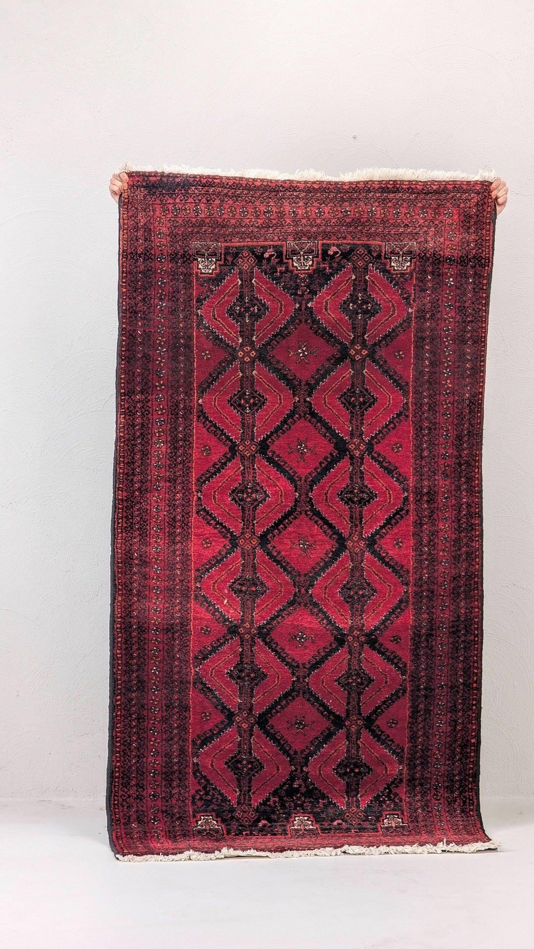 Hand holding vintage red Persian rug with geometric patterns against white wall