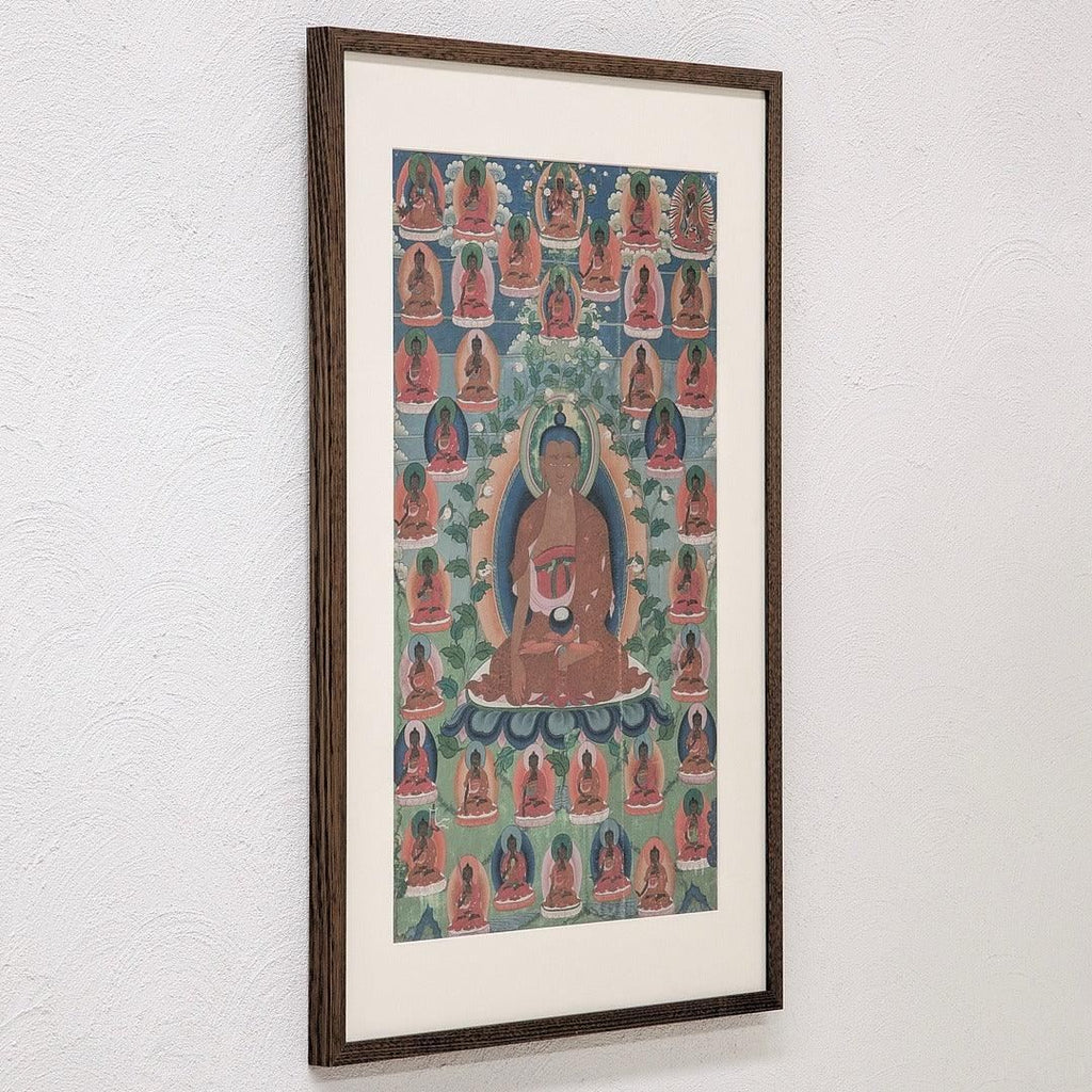 Framed Buddhist thangka painting with multiple Buddhas on a white textured wall