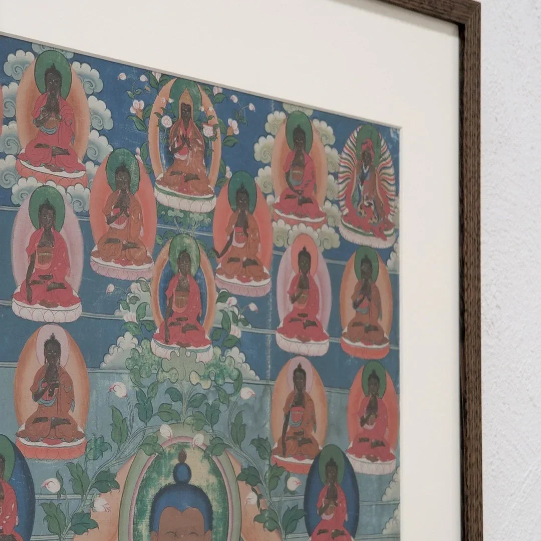 Framed Tibetan thangka painting with multiple seated Buddhas on a wall