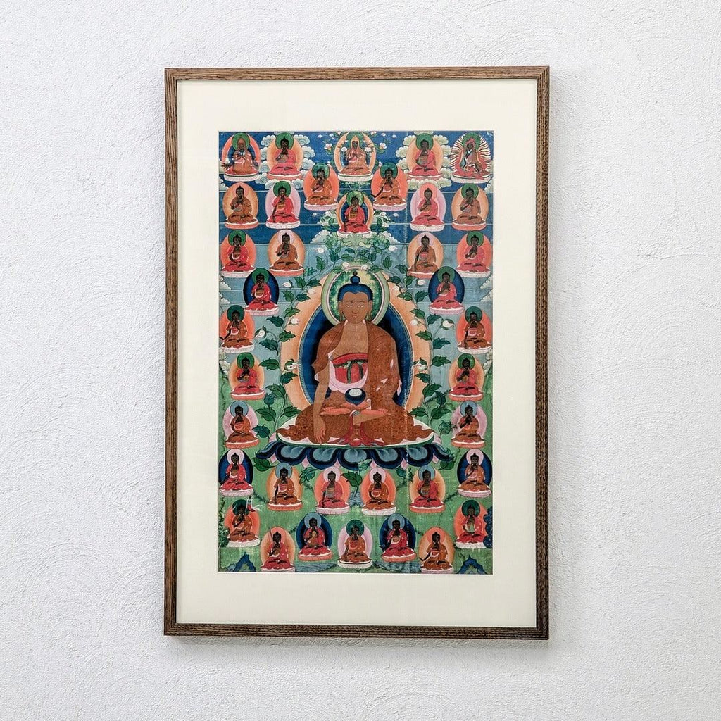 Framed Buddhist thangka artwork featuring seated Buddha and multiple smaller Buddhas on wall