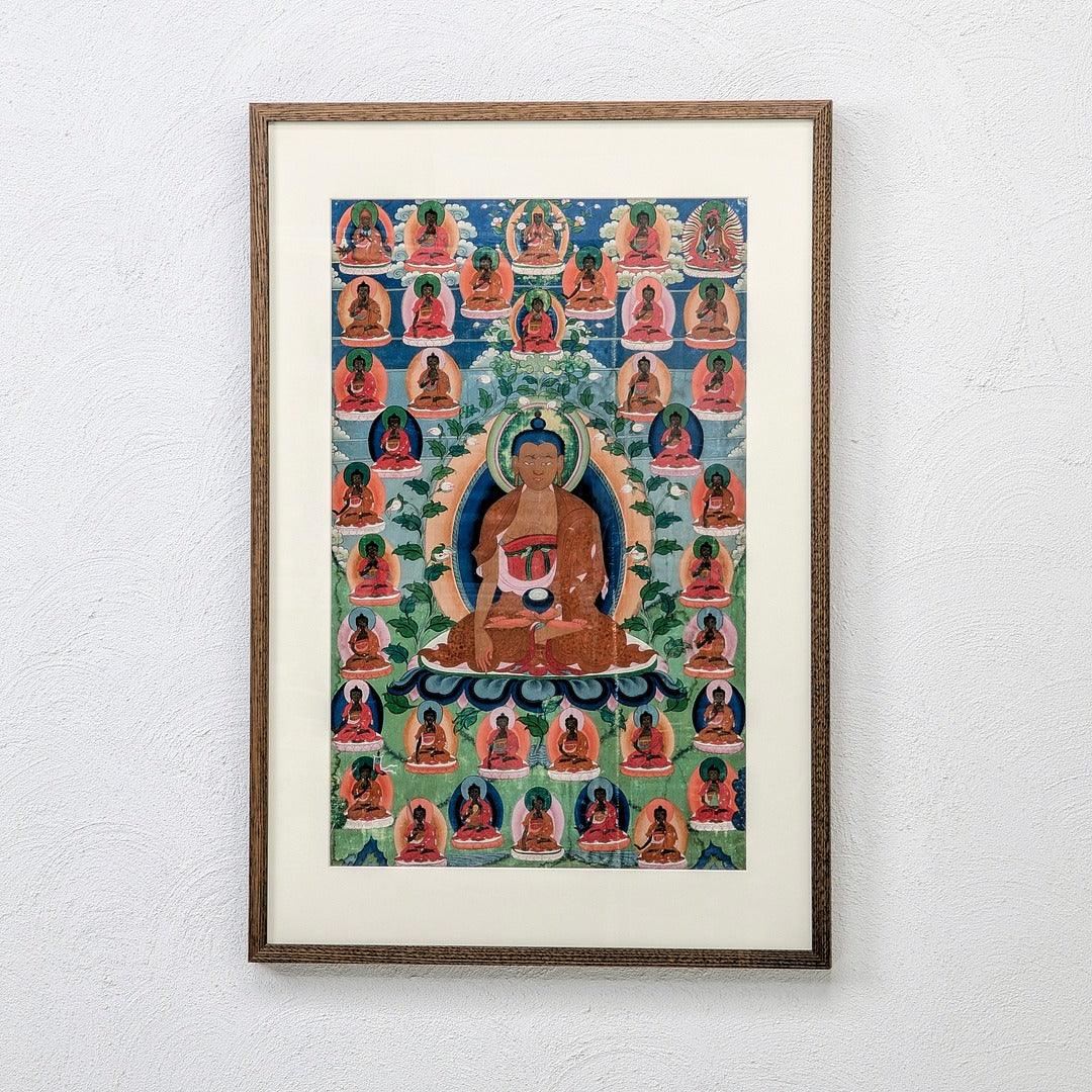 Framed Buddhist thangka artwork featuring seated Buddha and multiple smaller Buddhas on wall