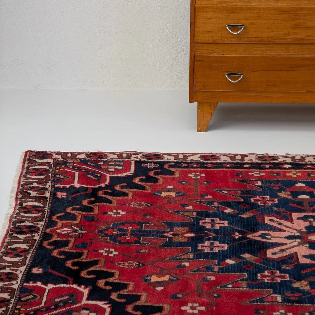 Vintage red and navy patterned rug with geometric design next to mid-century wooden dresser