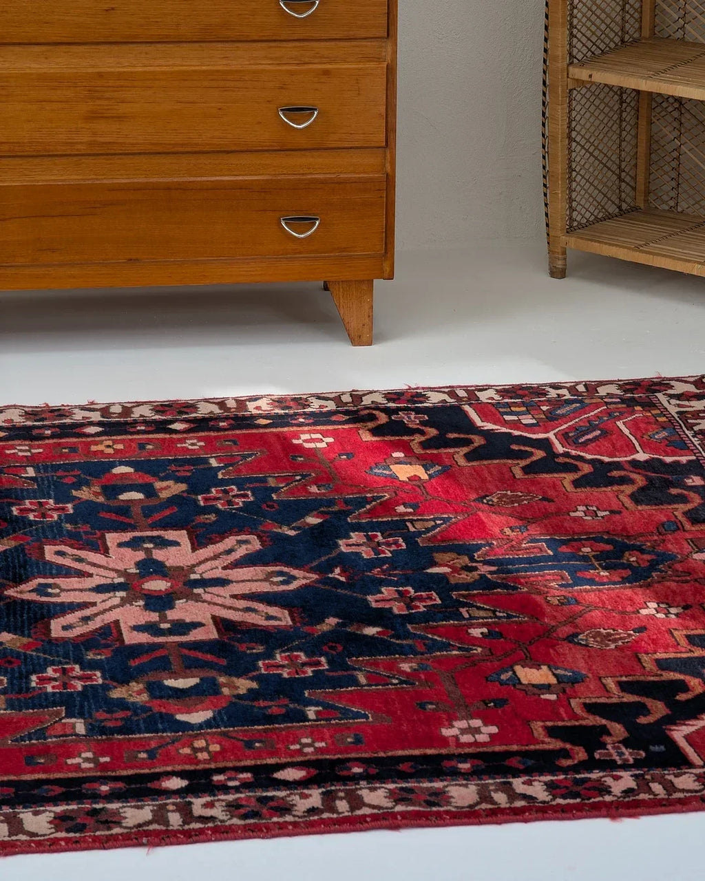 Colorful red and navy vintage rug with geometric patterns beside mid-century wooden dresser