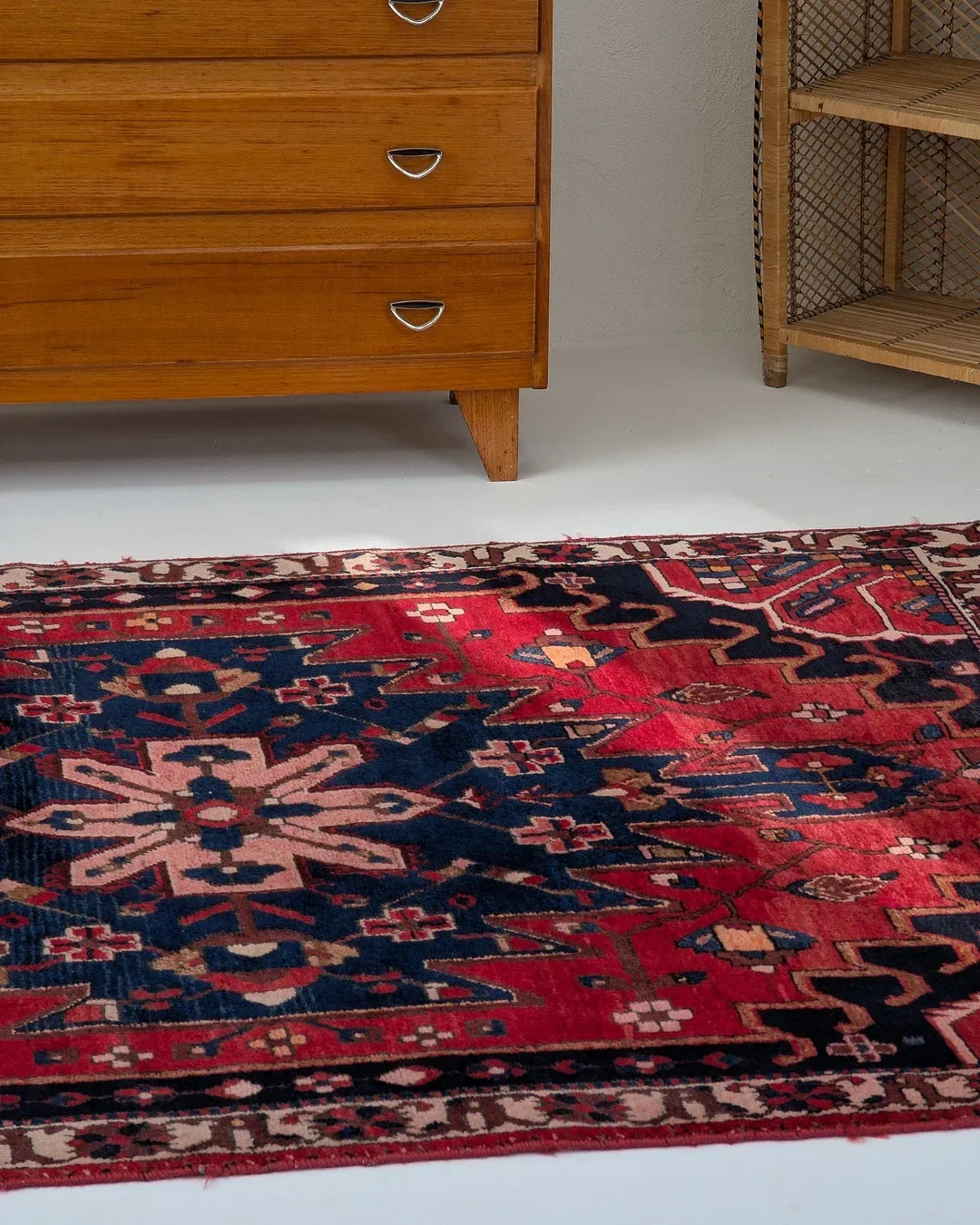 Colorful red and navy vintage rug with geometric patterns beside mid-century wooden dresser