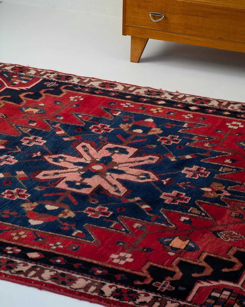 Vintage Persian rug with red and navy geometric floral pattern beside mid-century wood furniture