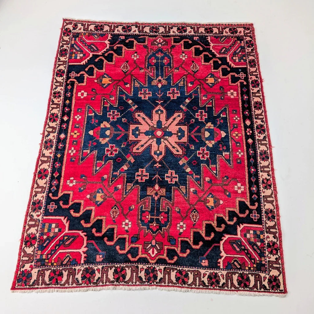 Vintage Persian rug with bold geometric patterns in red, navy, and beige on a white background