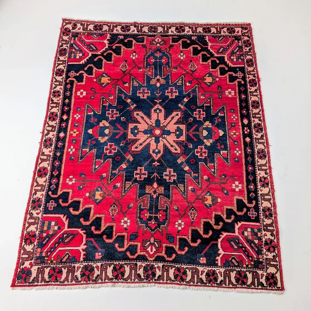 Vintage Persian rug with bold geometric patterns in red, navy, and beige on a white background
