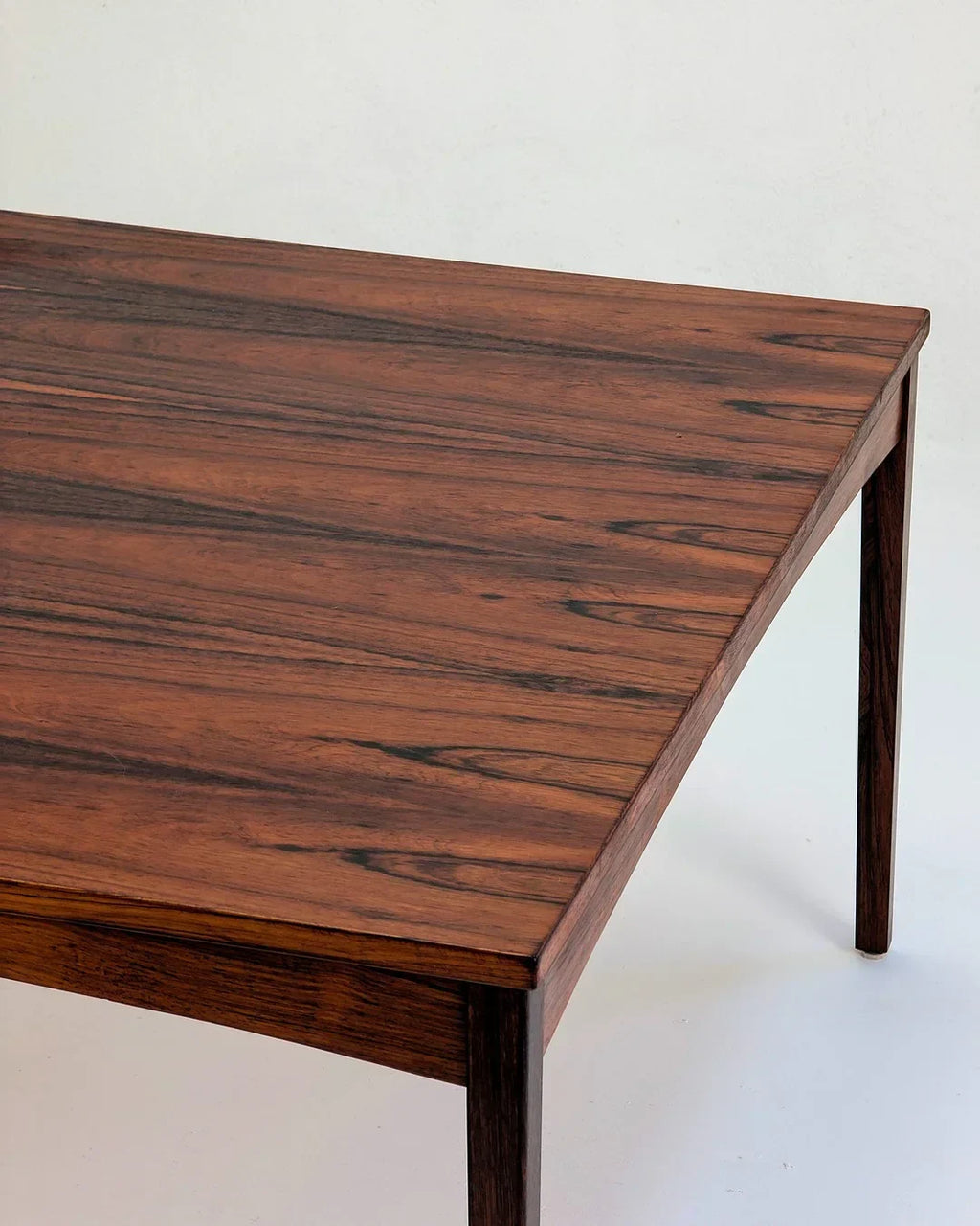 Mid-century modern rectangular rosewood dining table with rich grain detail against white background