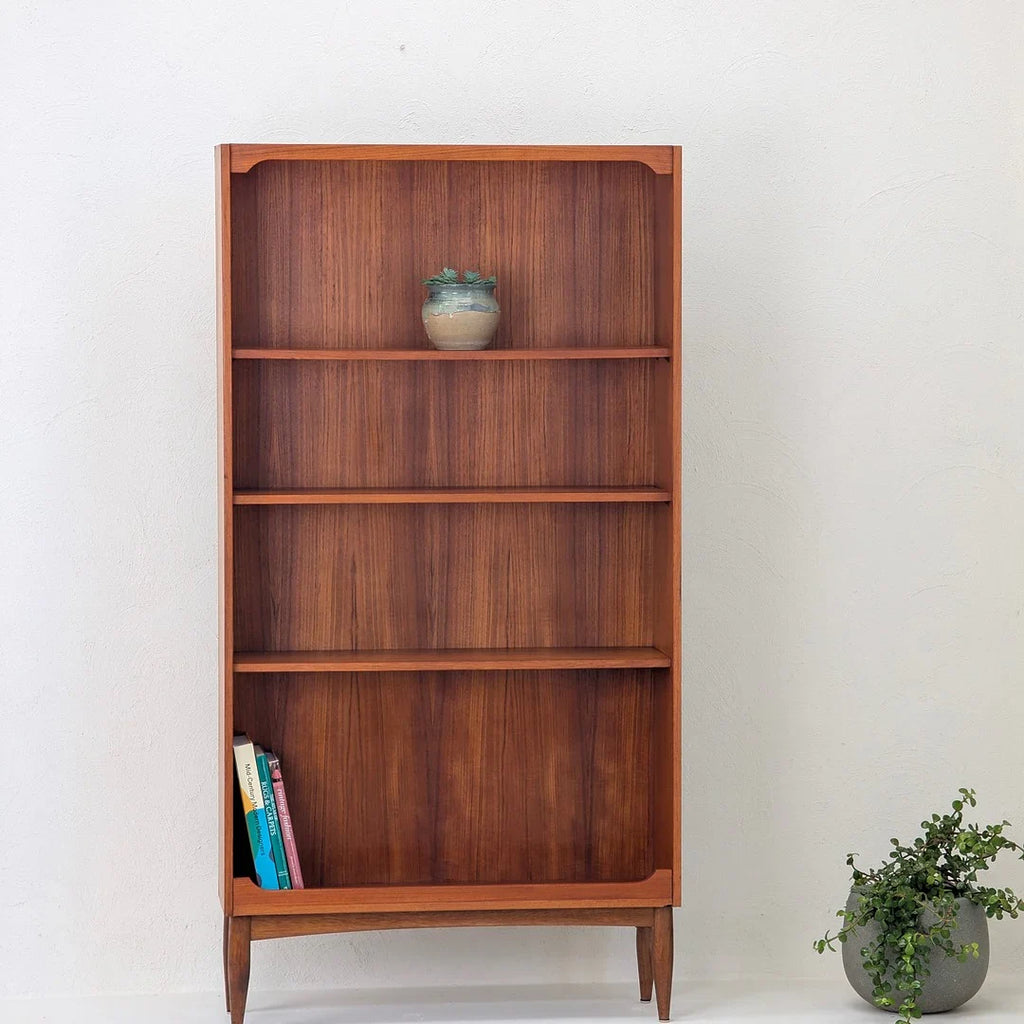Minimalist wooden bookshelf with four shelves, small plant pot on top shelf, and books at bottom