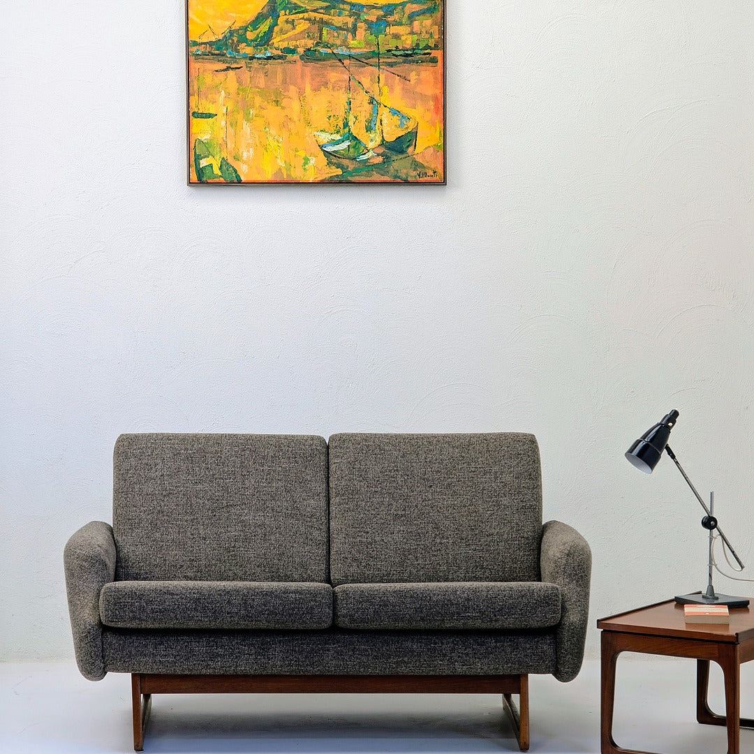 Minimalist living room with gray mid-century sofa, wooden side table, black desk lamp, and vibrant yellow wall painting