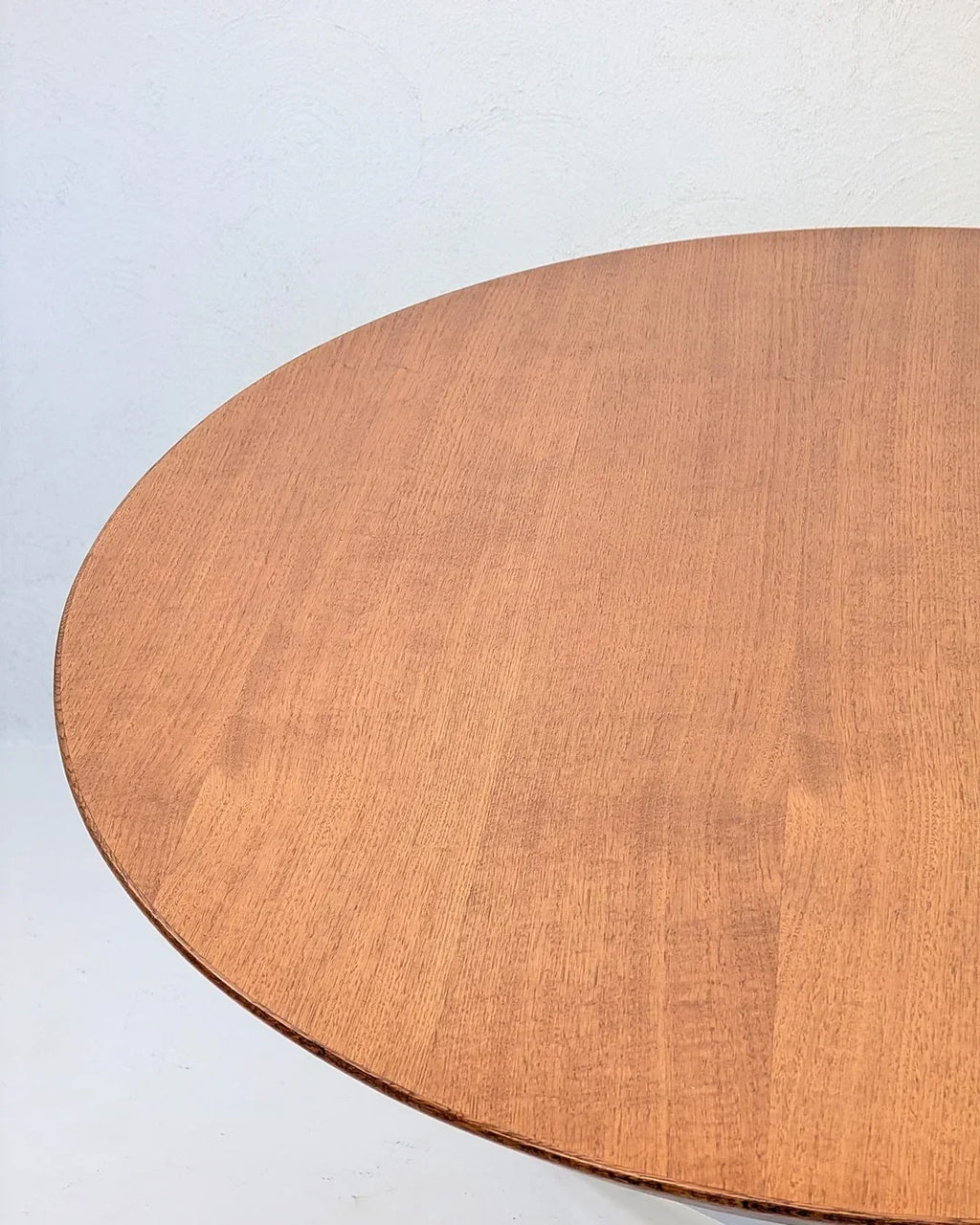 Round wooden table with light brown finish against a white textured wall