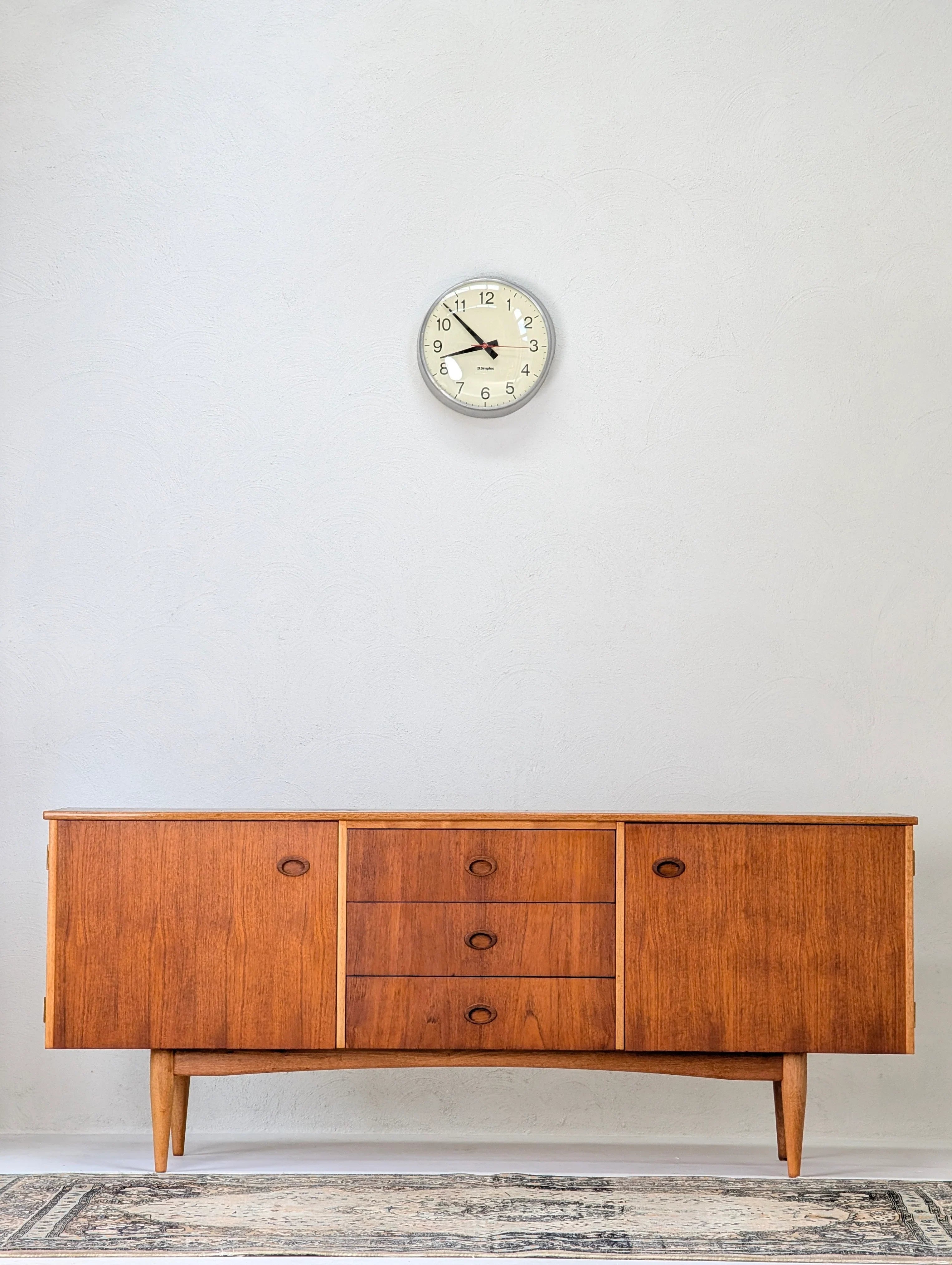 Mid-century modern wooden sideboard with drawers and cabinets under a round wall clock on white textured wall
