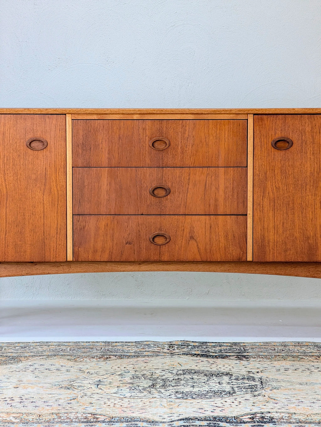 Mid-century modern wooden sideboard with three drawers and two cabinets on a patterned rug