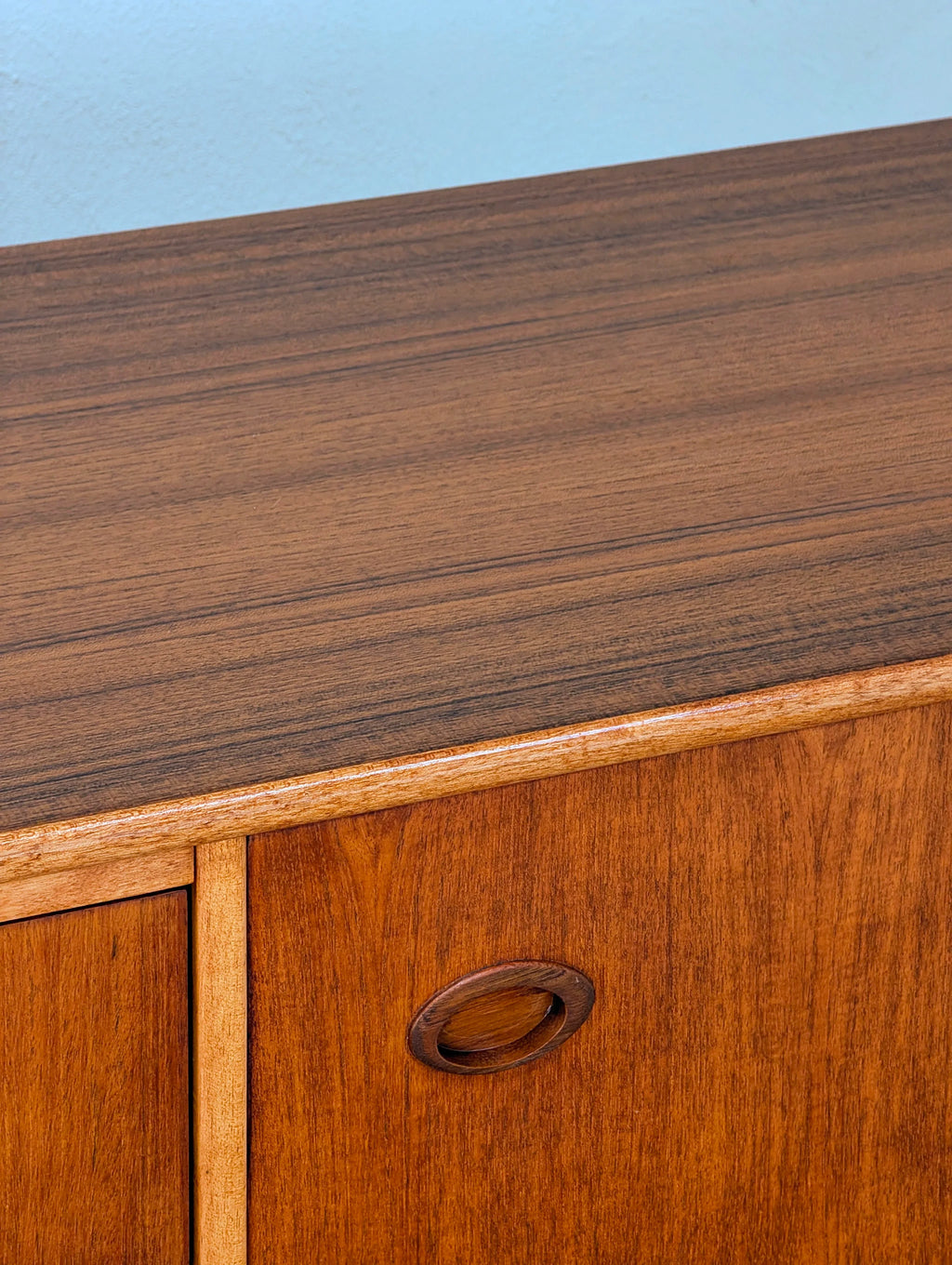 Close-up of wooden cabinet with oval recessed handle against light blue wall