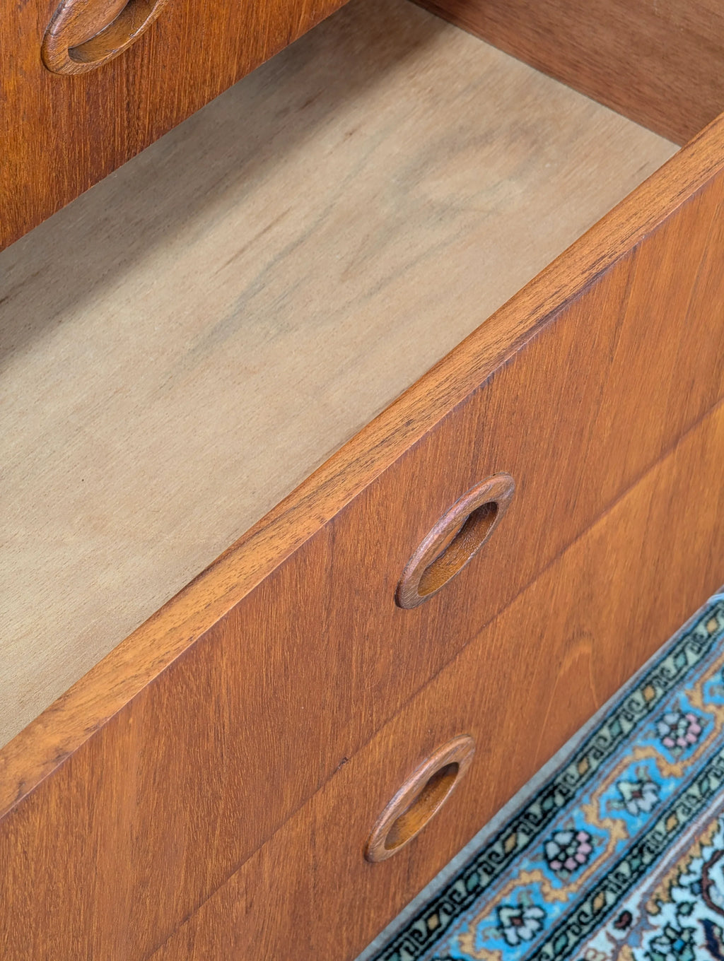 Open wooden mid-century drawer with round handles on patterned blue rug