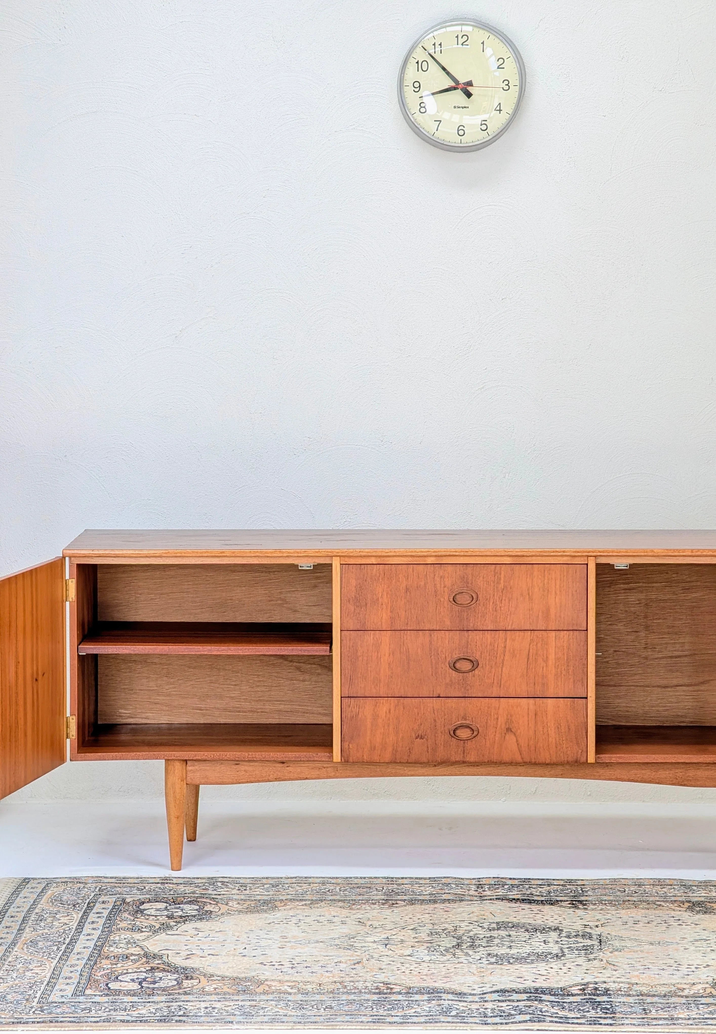 Mid-century modern wooden sideboard with open shelves and drawers on white wall with round clock