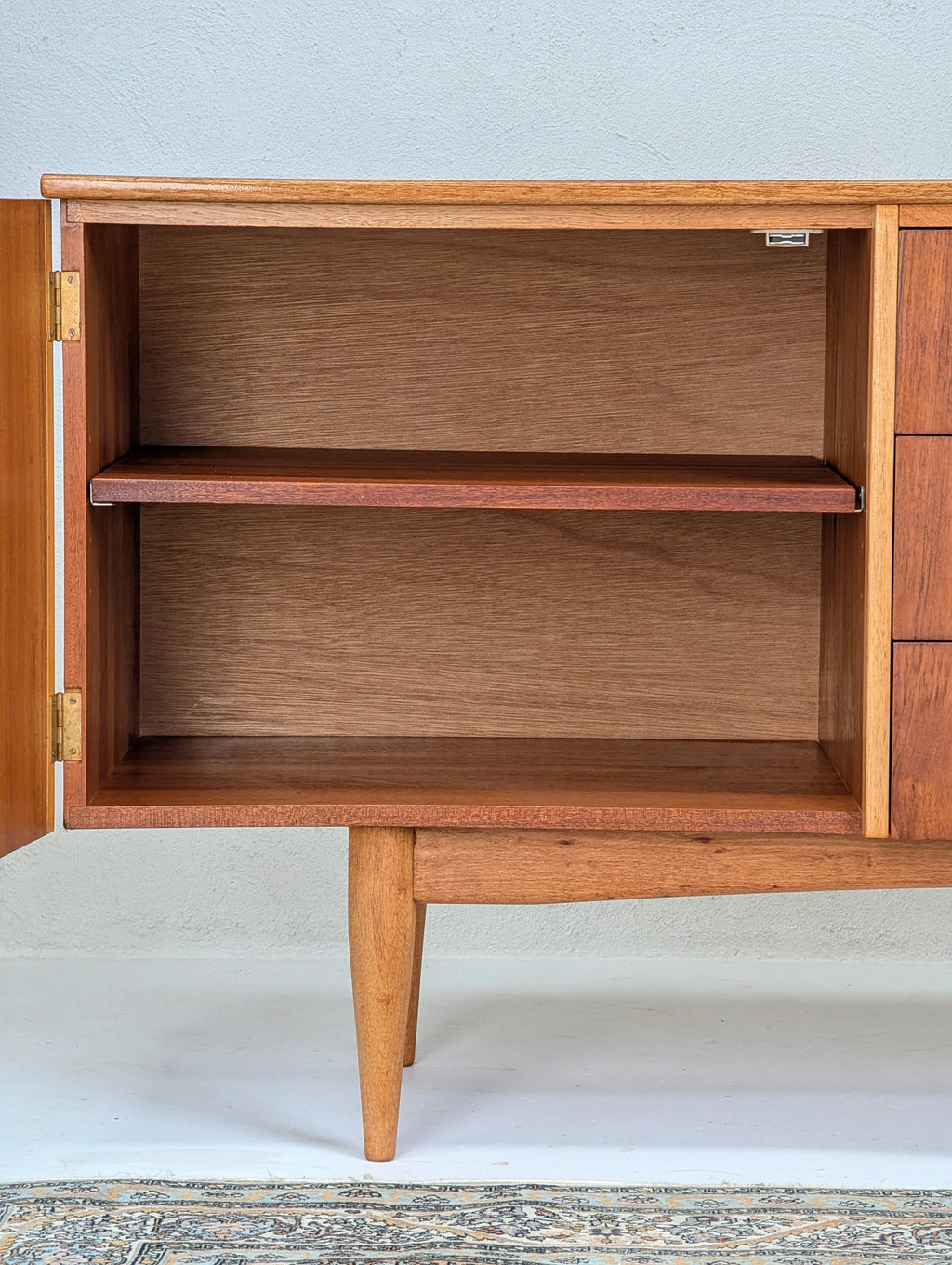 Open wooden mid-century modern cabinet with shelf and tapered legs on patterned rug