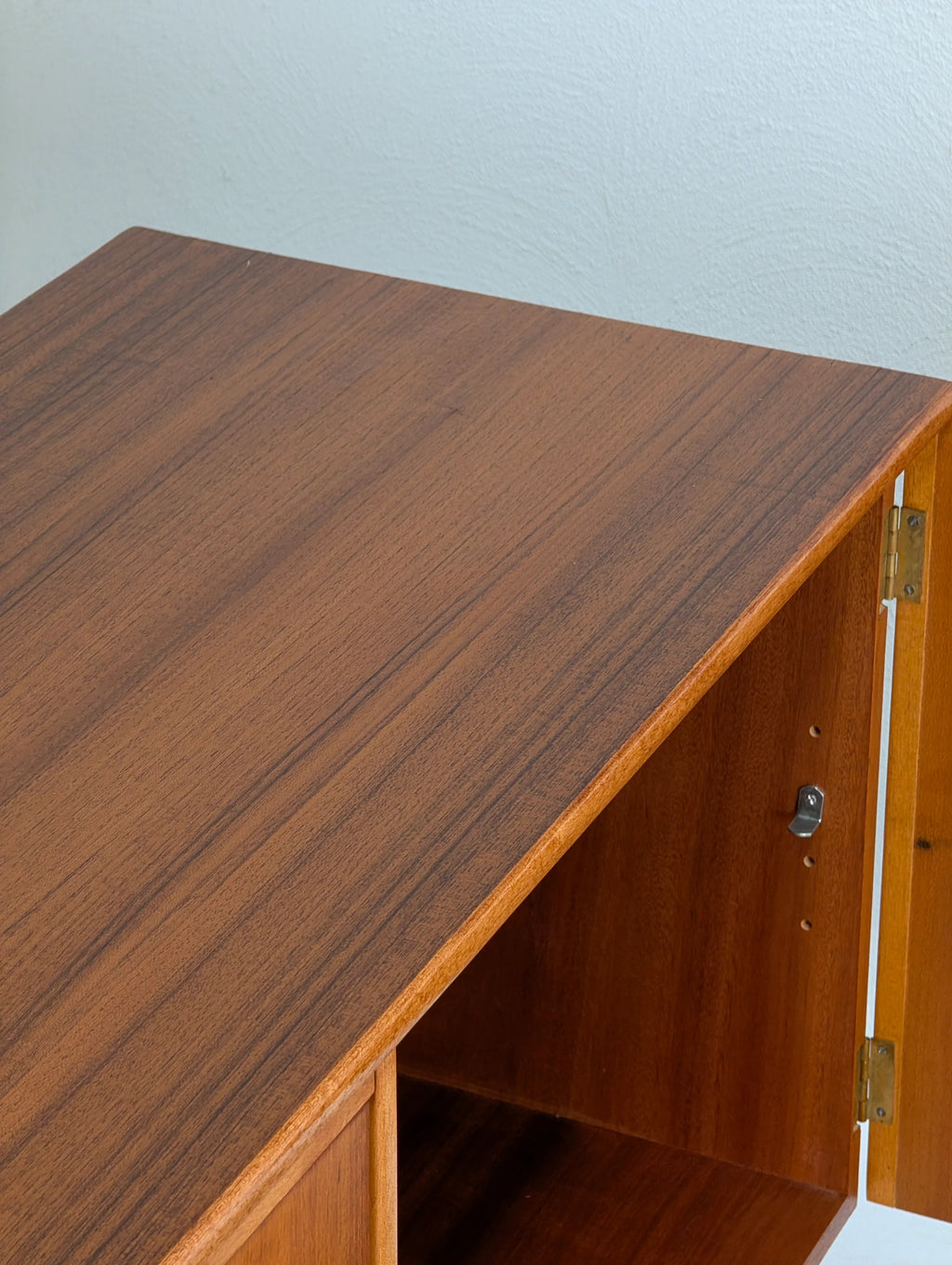 Open wooden cabinet with rich brown finish and a brass hinge against a white textured wall