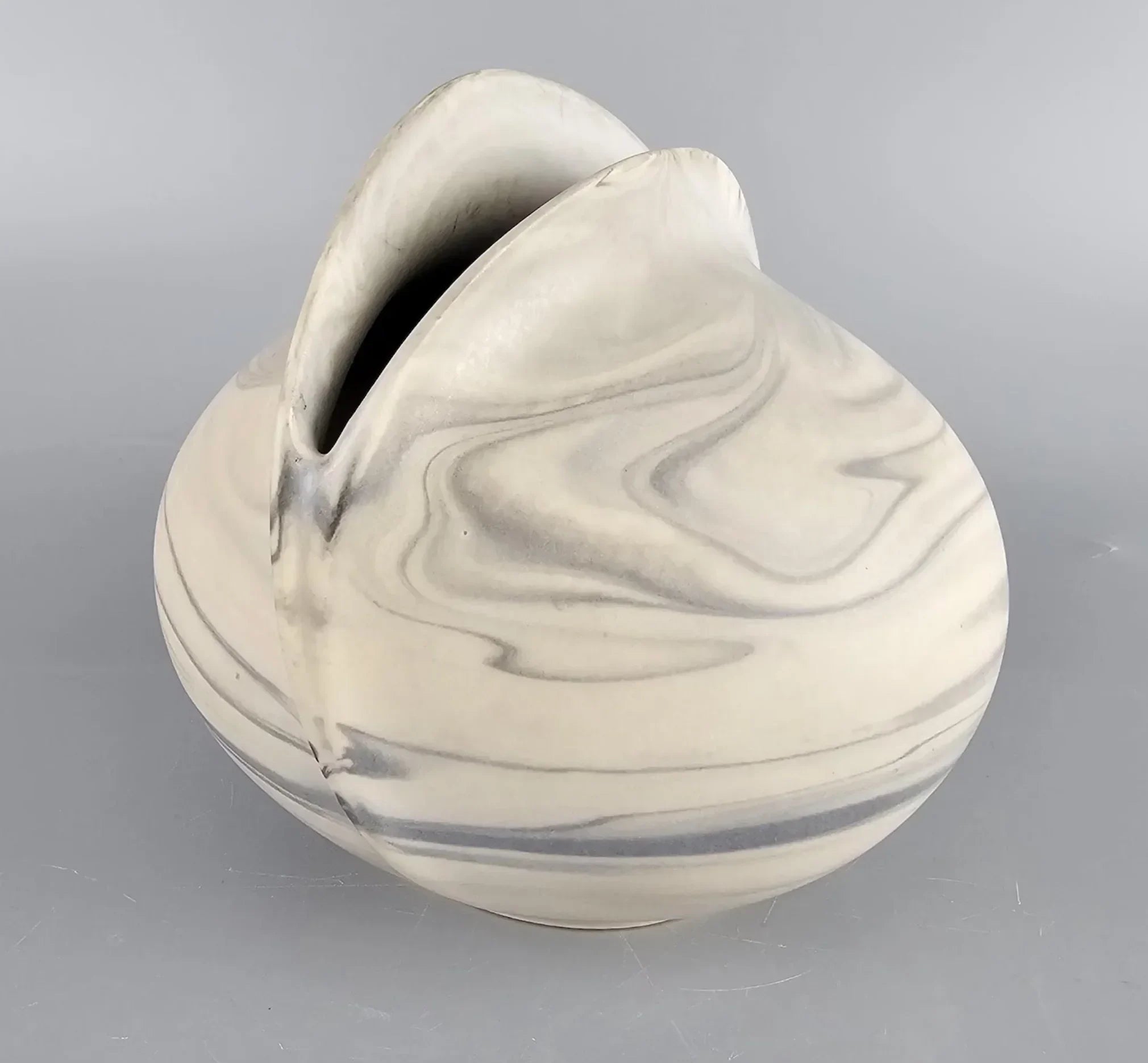 Marbled ceramic vase with organic curves and swirled gray patterns, set on a gray background.