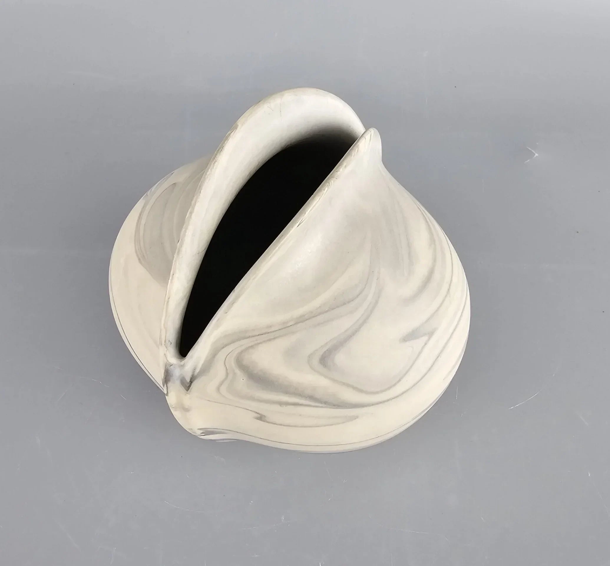 Modern marbled ceramic vase with abstract opening on a grey background