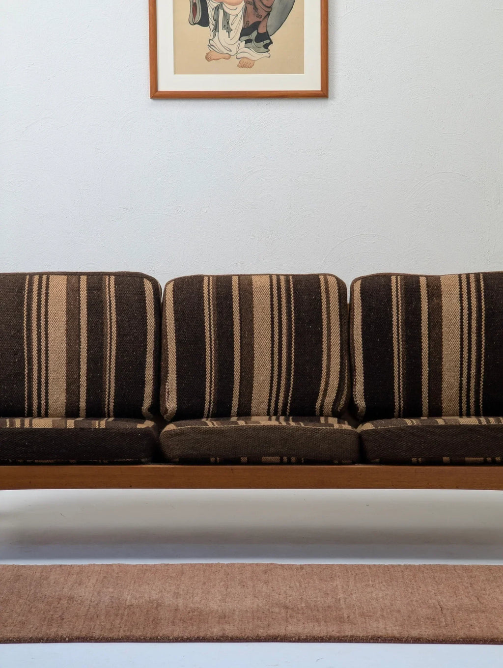 Mid-century brown striped sofa with a beige rug and framed artwork on white wall