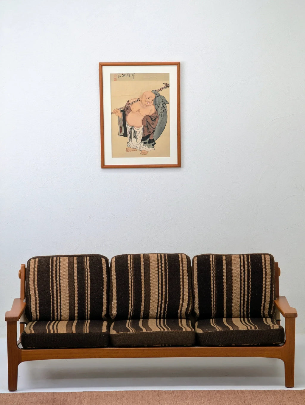 Vintage striped sofa below framed Asian art on white wall in minimalist living room