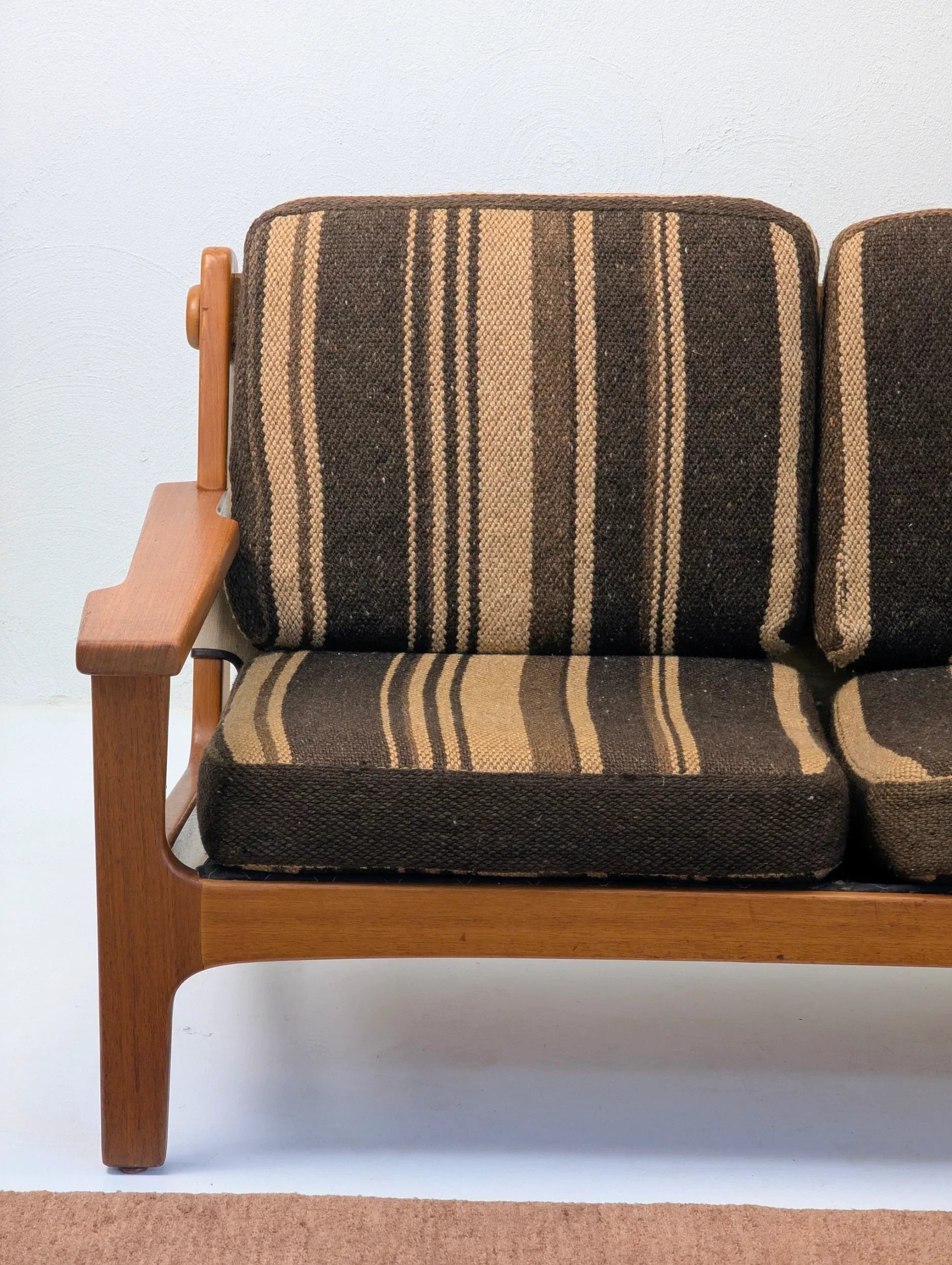 Mid-century modern wooden armchair with brown striped cushions against white wall