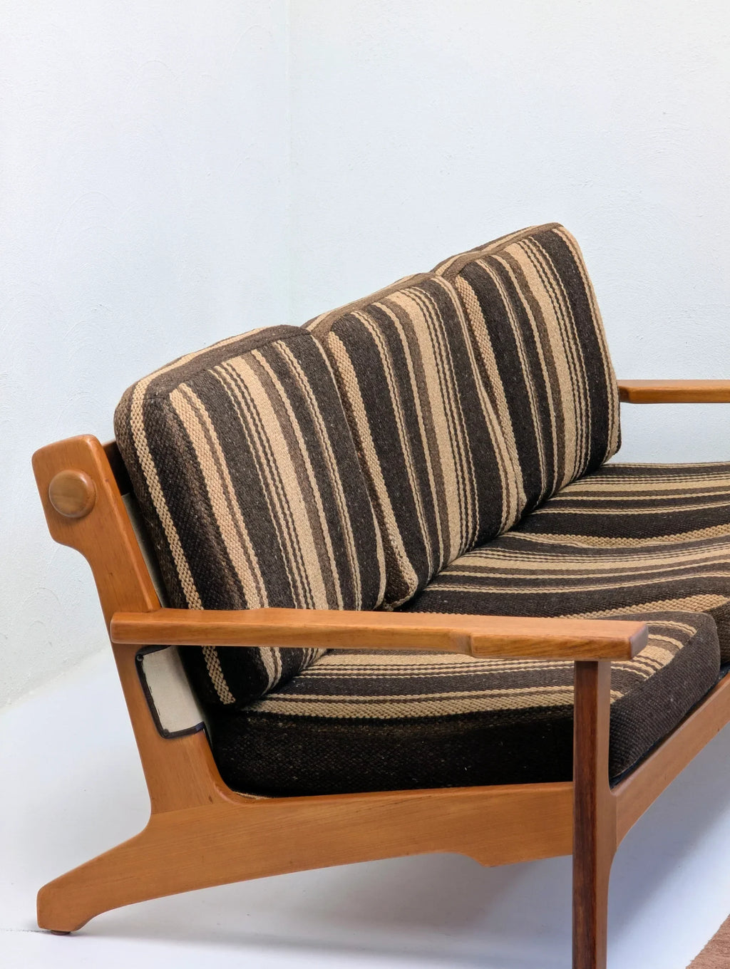 Mid-century modern wooden sofa with striped brown and beige cushions against white wall