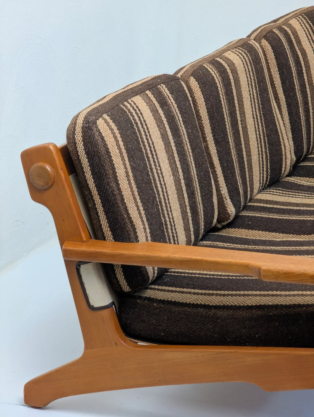Mid-century modern wooden sofa with brown striped cushions against a light wall