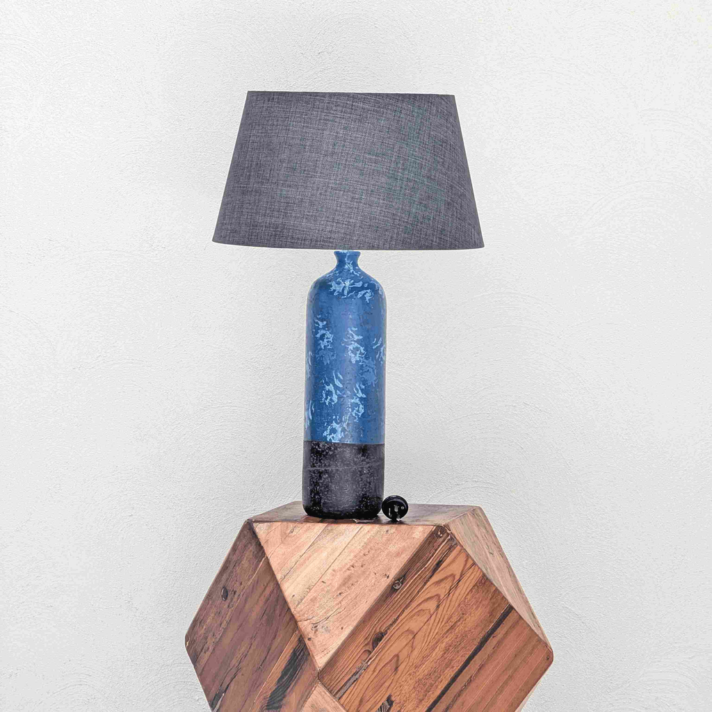 Table lamp with blue base and black shade on a wooden block against a white background

