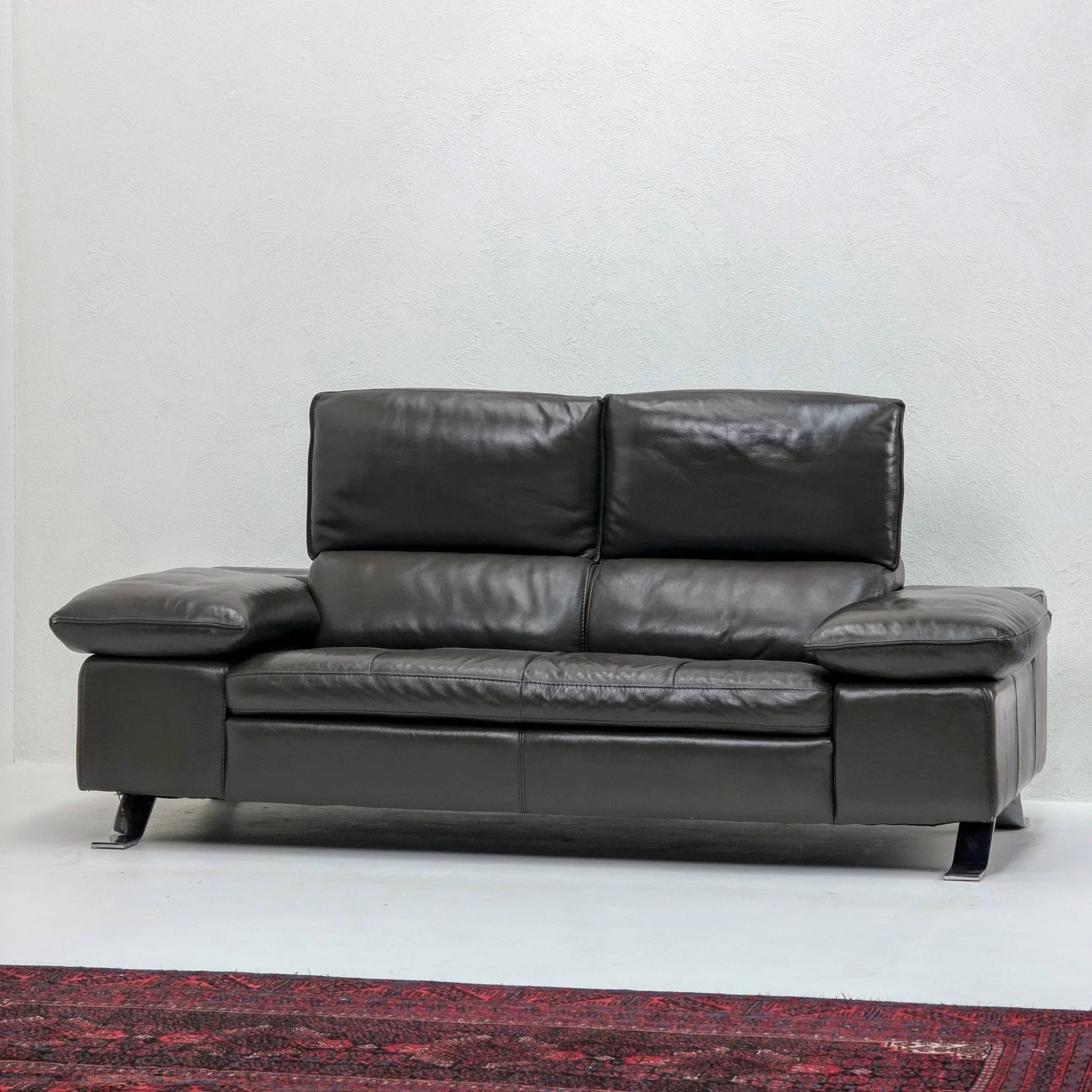 Domicil Butterfly black leather sofa with wide arms on white wall and red rug