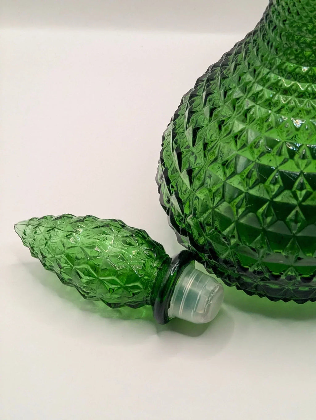 Green diamond point glass genie bottle decanter with matching stopper on white surface