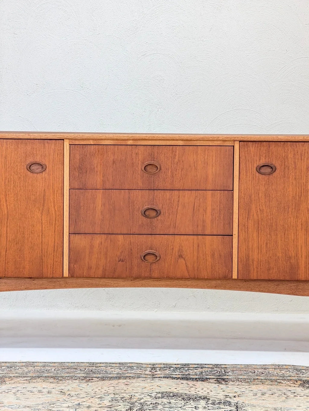 Mid-century teak sideboard with drawers and cabinets against a textured white wall