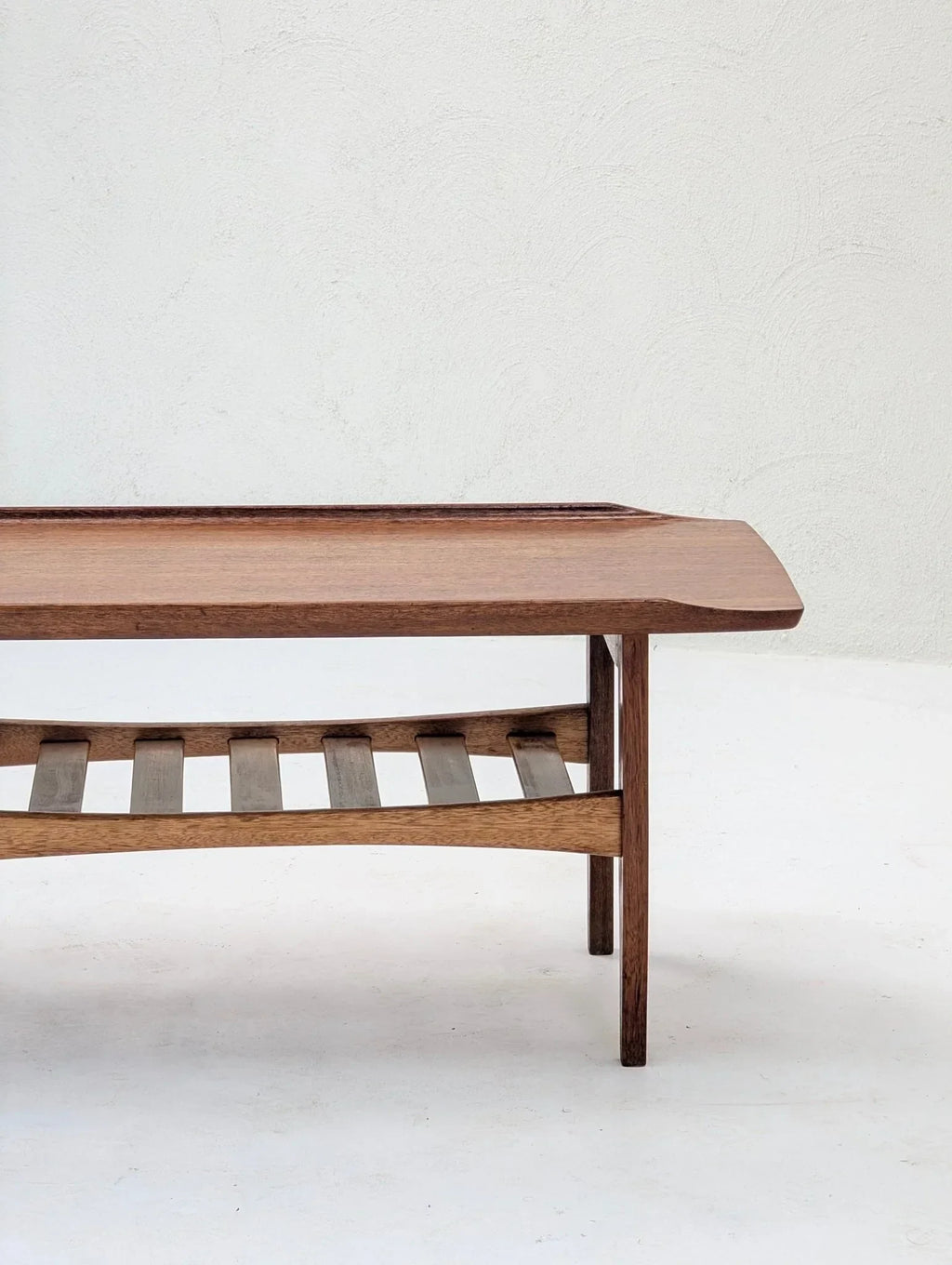 Italian solid teak tray top coffee table with slatted shelf against a white textured wall