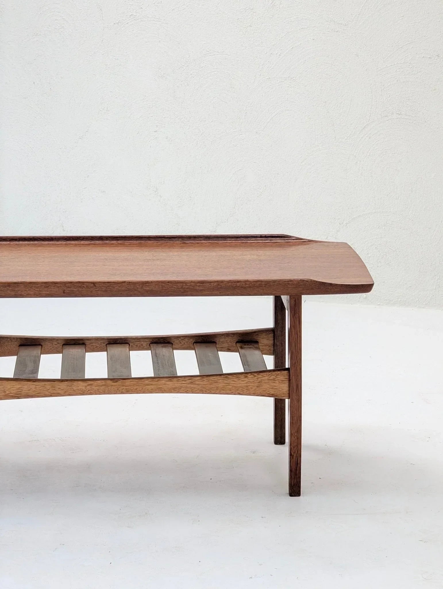 Italian solid teak tray top coffee table with slatted shelf against a white textured wall