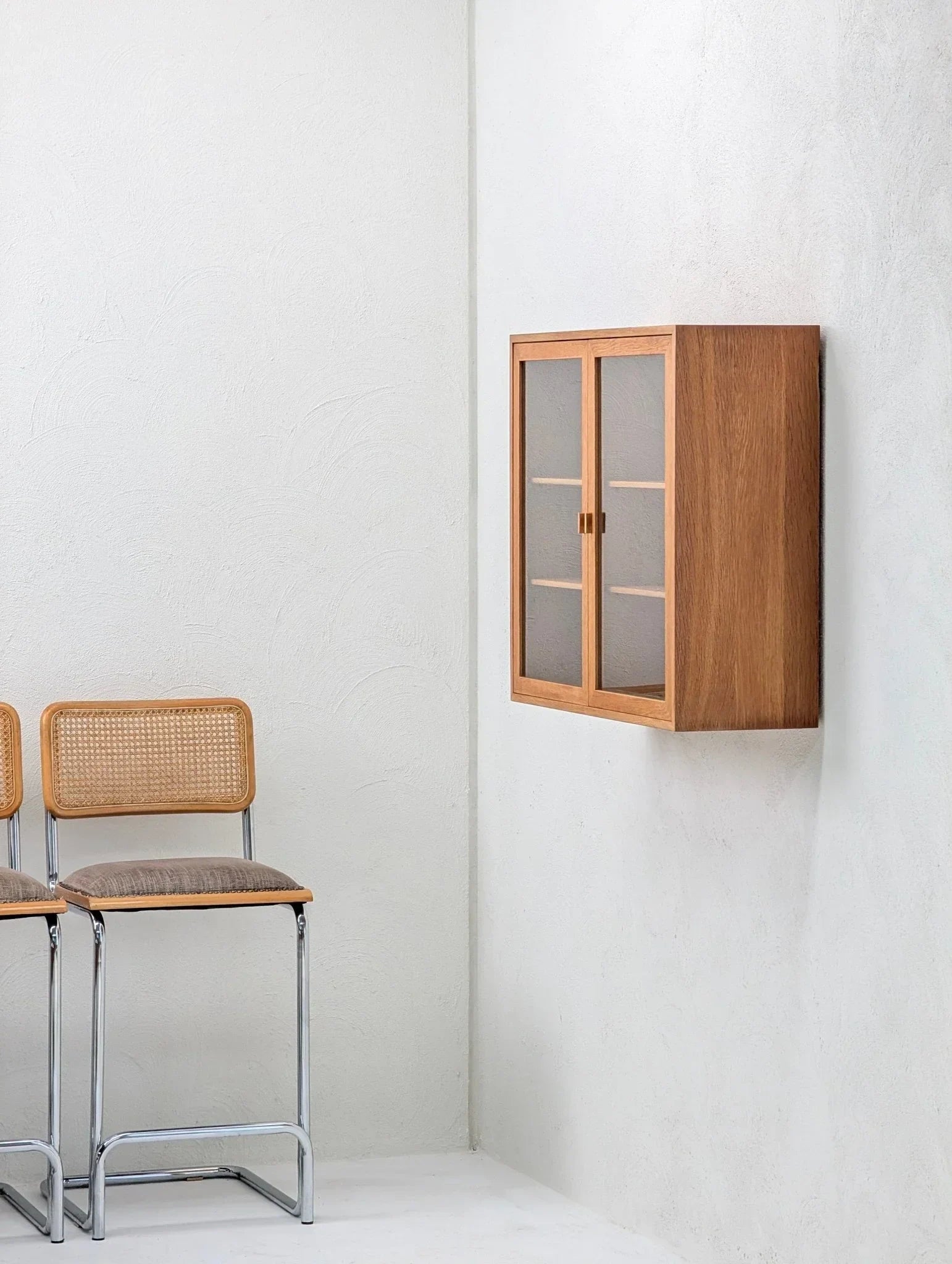 Mid-century oak and glass wall display cabinet with cane chairs in minimalist room