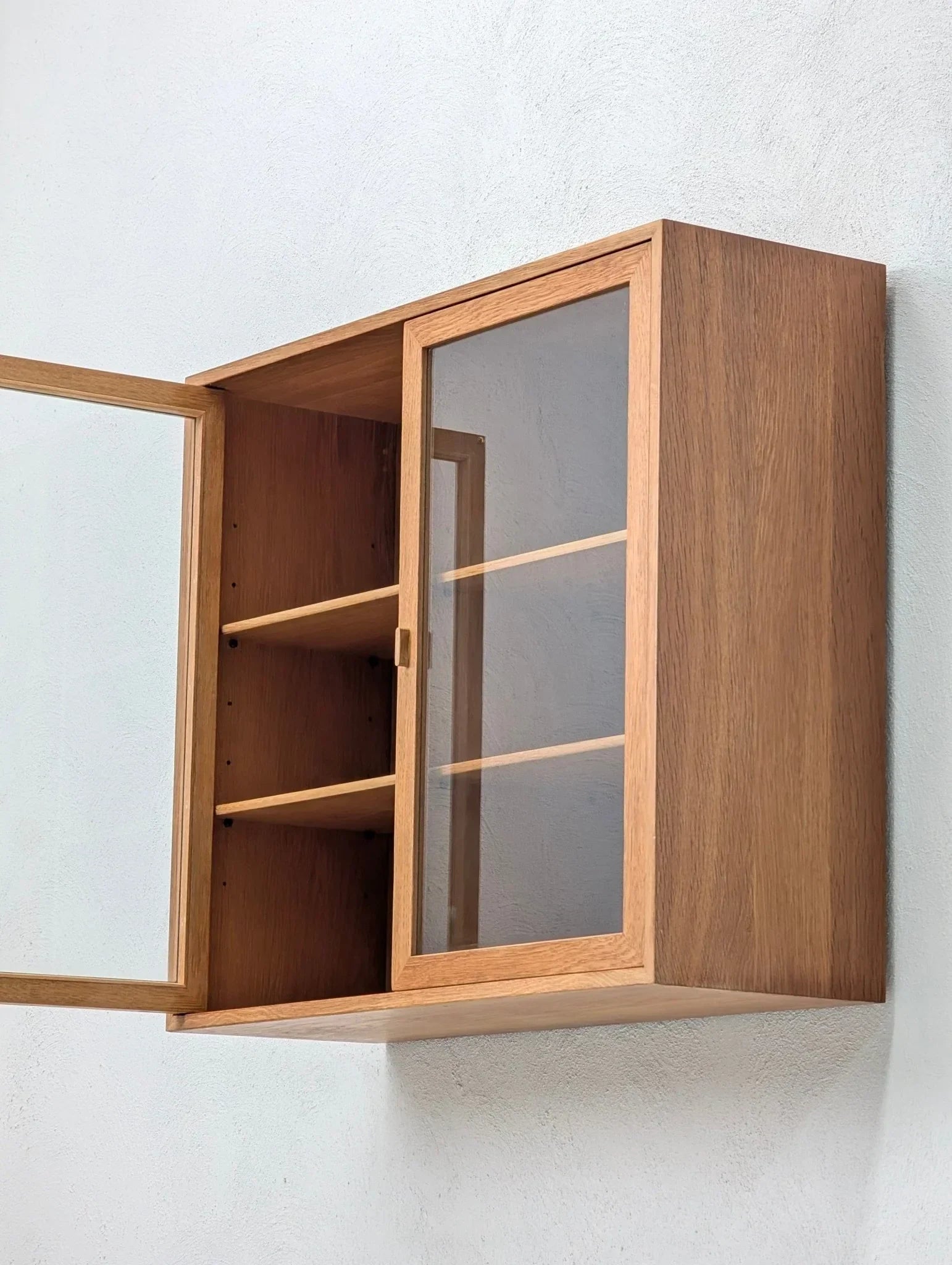 Mid-century Danish oak and glass display cabinet with open door, wall-mounted on white wall