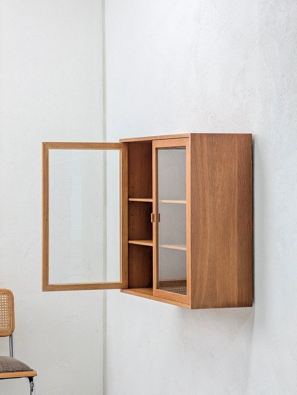 Mid-century Danish oak and glass display cabinet mounted on a white wall, open door