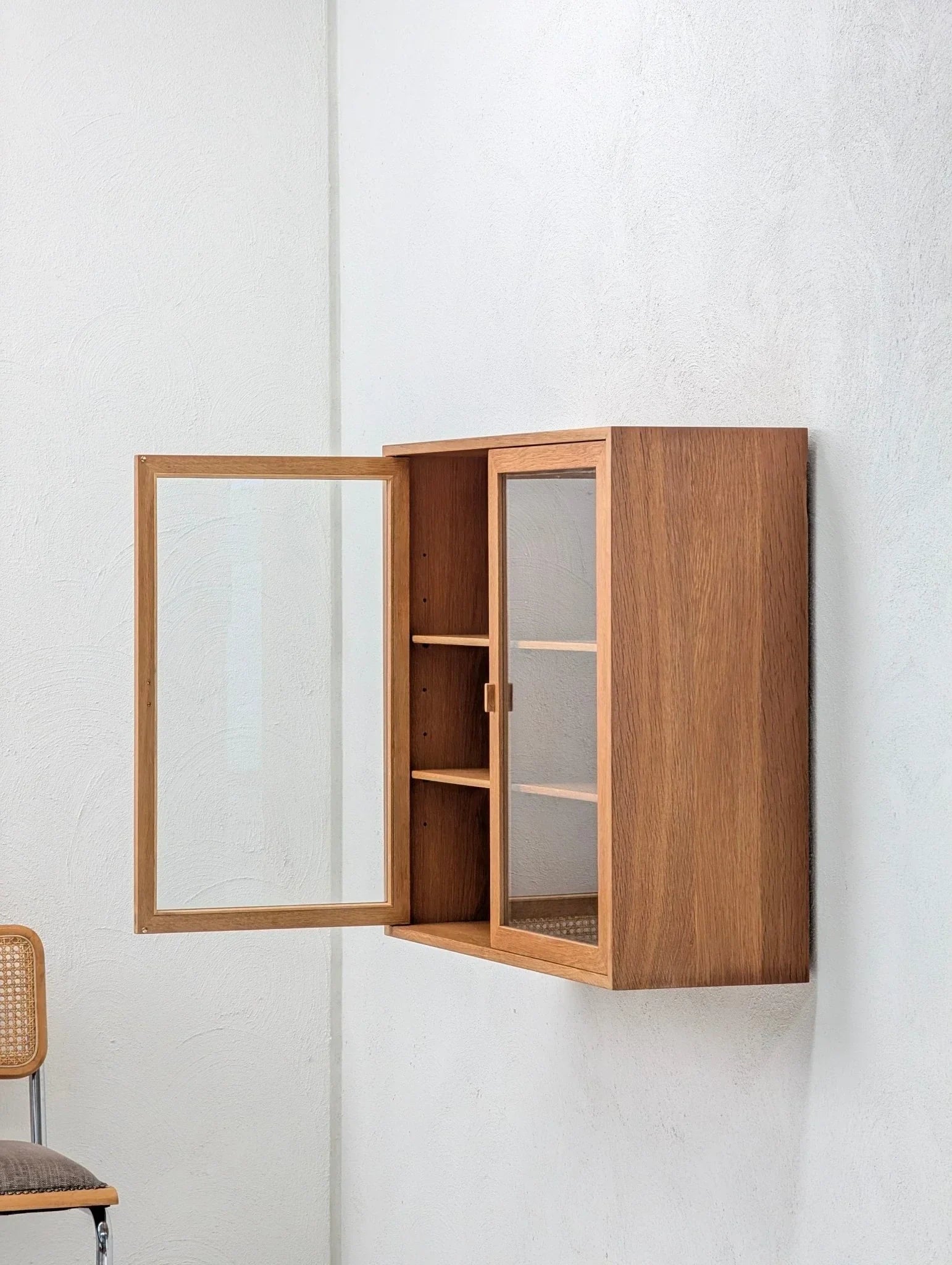 Mid-century Danish oak and glass display cabinet mounted on a white wall, open door