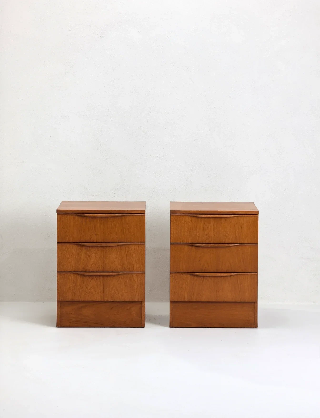 Pair of mid-century teak bedside tables with three drawers on a white background