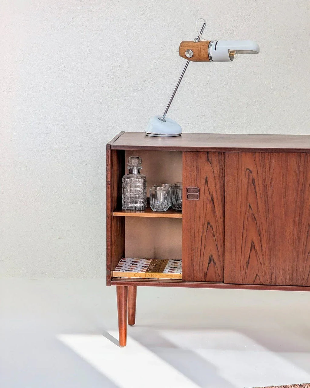 Mid-century Danish teak cabinet with glassware, books, and vintage table lamp