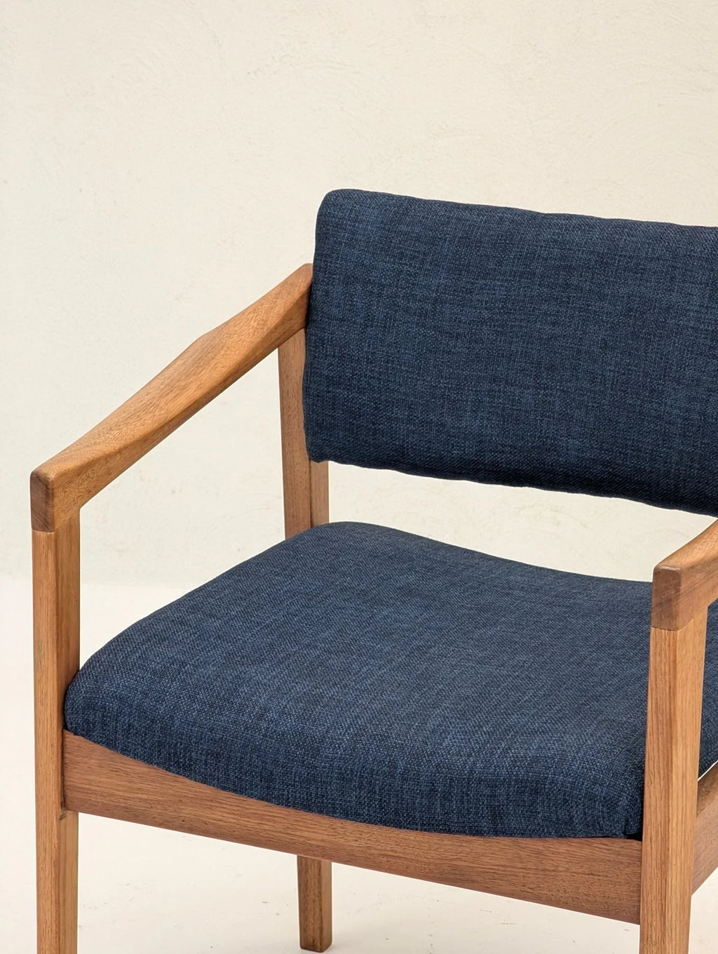 Mid-century modern armchair with navy blue fabric and wooden frame against light wall